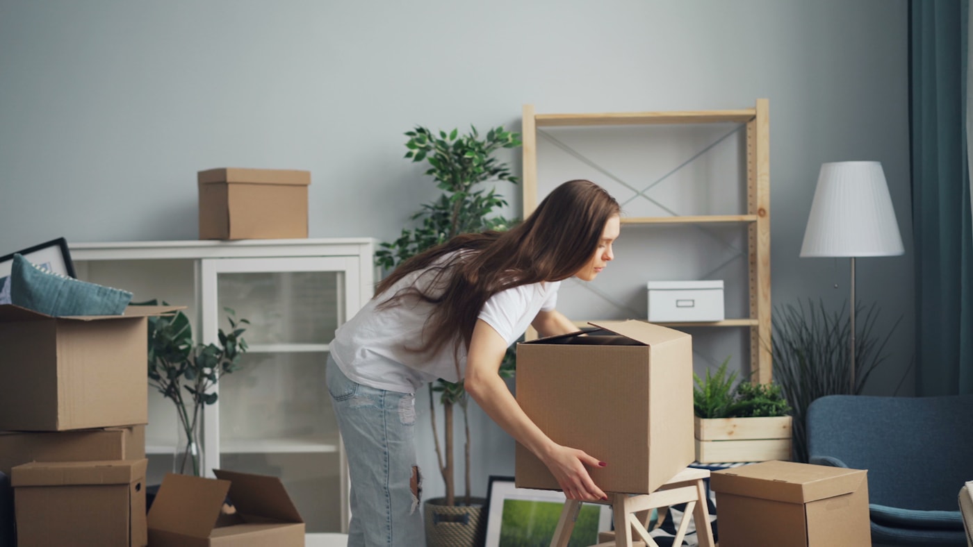 A person carefully packing a labeled moving box in a bright apartment